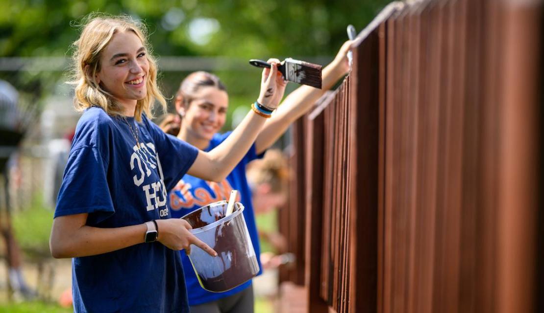 Student volunteers paint a fence as part of Humanics in Action